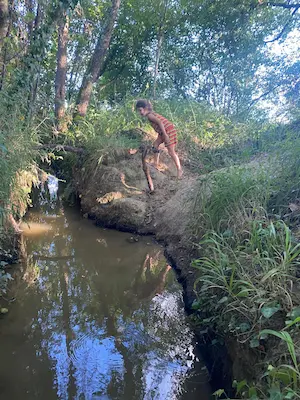 Enfant descendant vers un ruisseau en pleine nature sur le sentier pieds nus du Domaine de Larrous – Domaine de Larrous, Gaujacq (Landes)