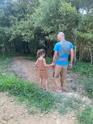 Adulte portant un bébé en écharpe de portage marchant avec un enfant sur le sentier pieds nus du Domaine de Larrous – Domaine de Larrous, Gaujacq (Landes)