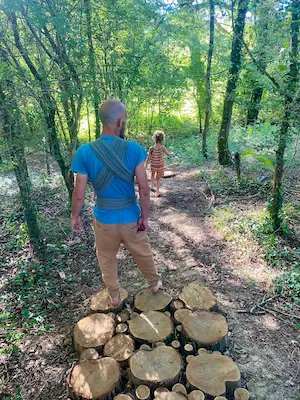 Famille marchant pieds nus en forêt sur des rondins de bois sur le sentier pieds nus du Domaine de Larrous – Domaine de Larrous, Gaujacq (Landes)